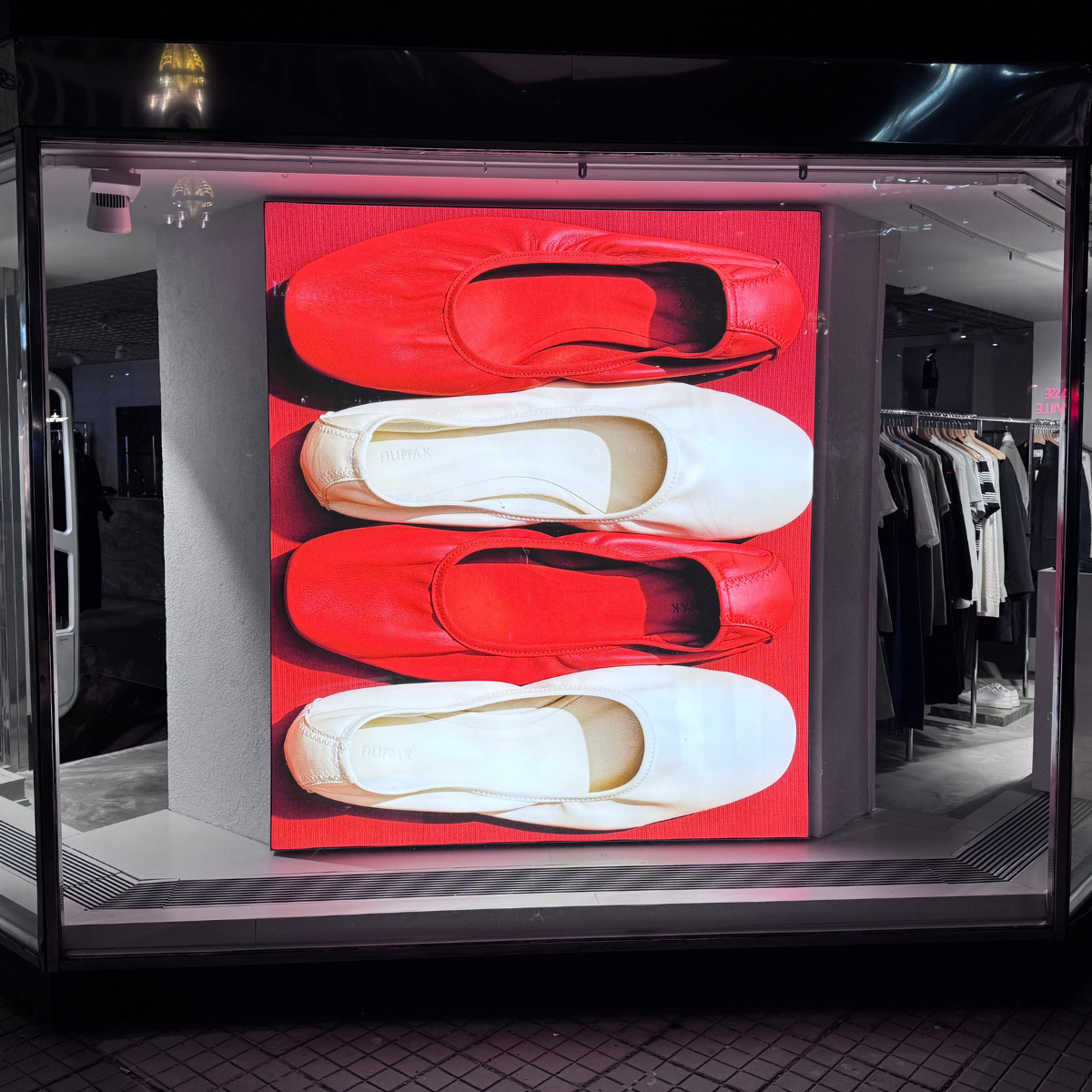 Storefront display with red and white flats stacked on a red panel; clothing racks visible inside the shop.