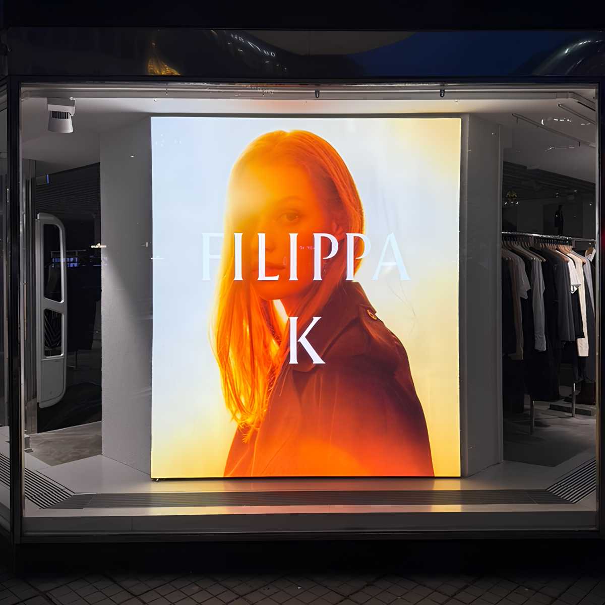 Backlit fashion store window poster showing a woman with an orange glow and the brand name FILIPPA K.