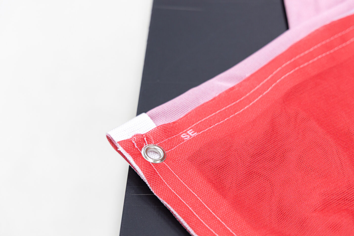 Close-up of red textured fabric with white stitched seams and a metal grommet on the edge, against a dark background.