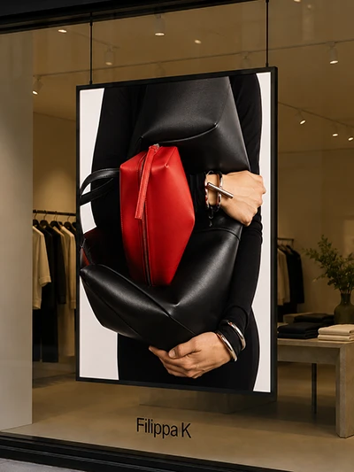 Store window poster of a person in black holding a red handbag and a black bag, with the Filippa K logo at the bottom.