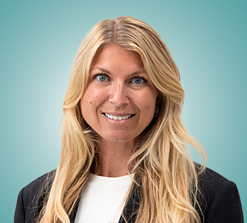 Head-and-shoulders portrait of a smiling blonde woman in a dark blazer and white top, with a teal gradient background.